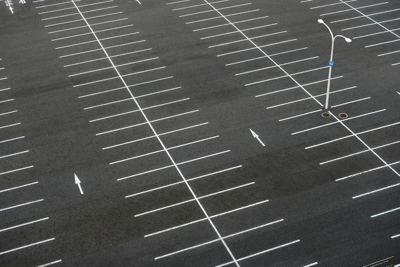 Weiße Stellplatzlinien und Richtungspfeile auf einem großen Asphaltparkplatz