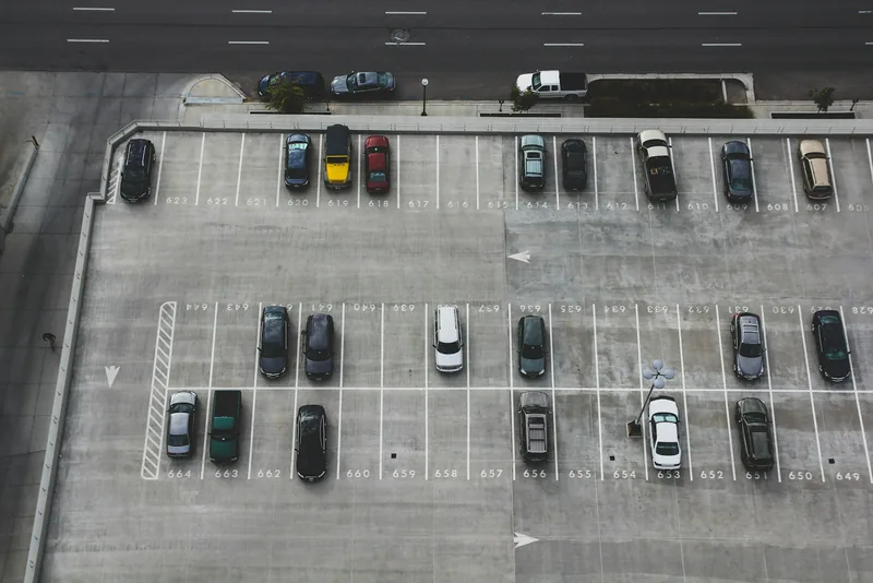 Von oben sichtbare Parkplatzreihen mit weißen Stellplatzlinien und einzelnen geparkten Autos